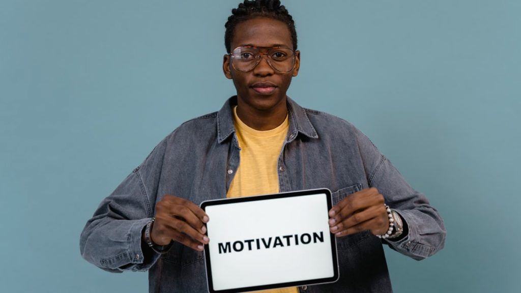 A young African American man holding a tablet displaying the word 'MOTIVATION' against a blue background.